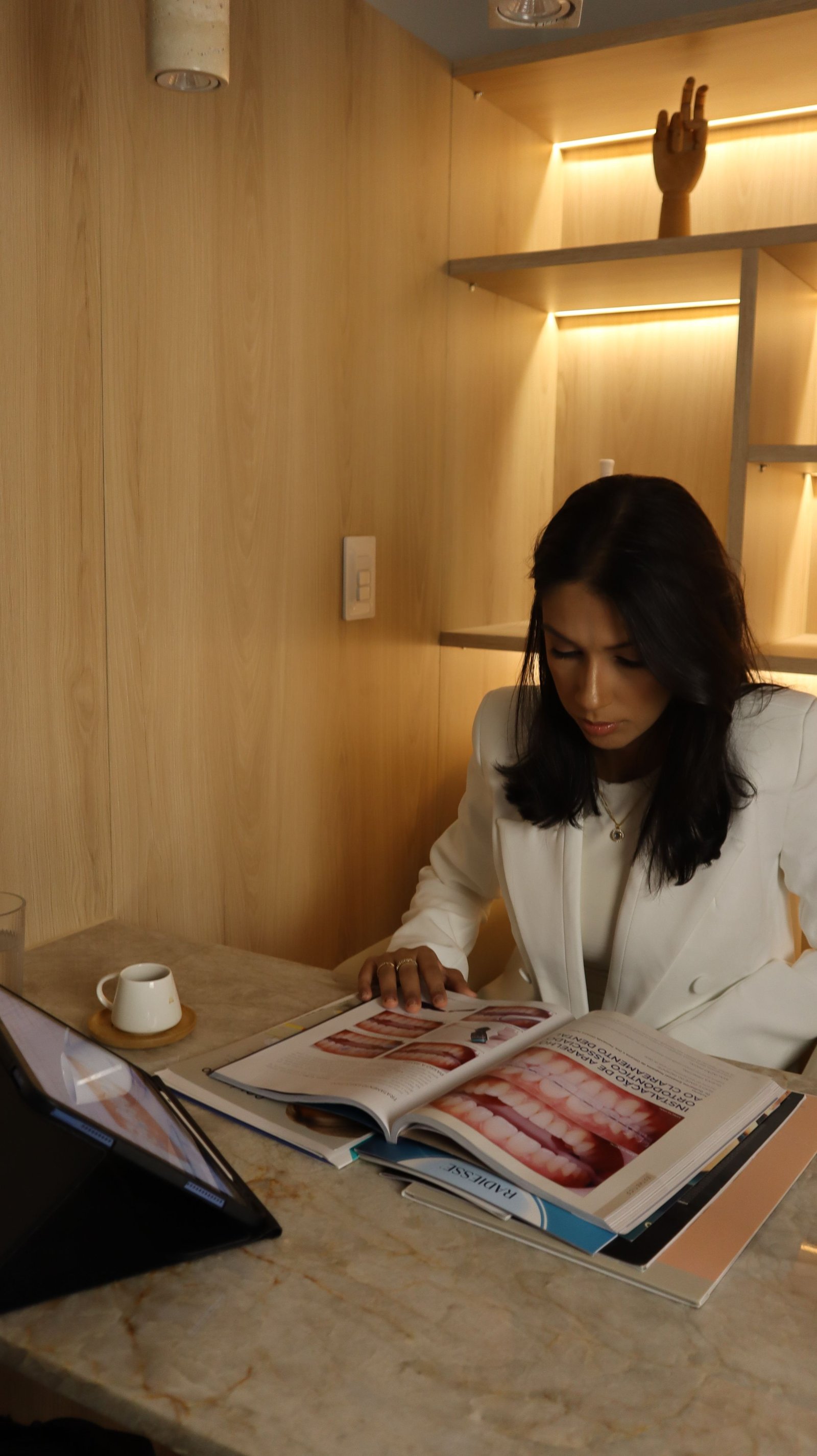 Dra. Débora com o olhar voltado para uma revista aberta sobre a mesa.